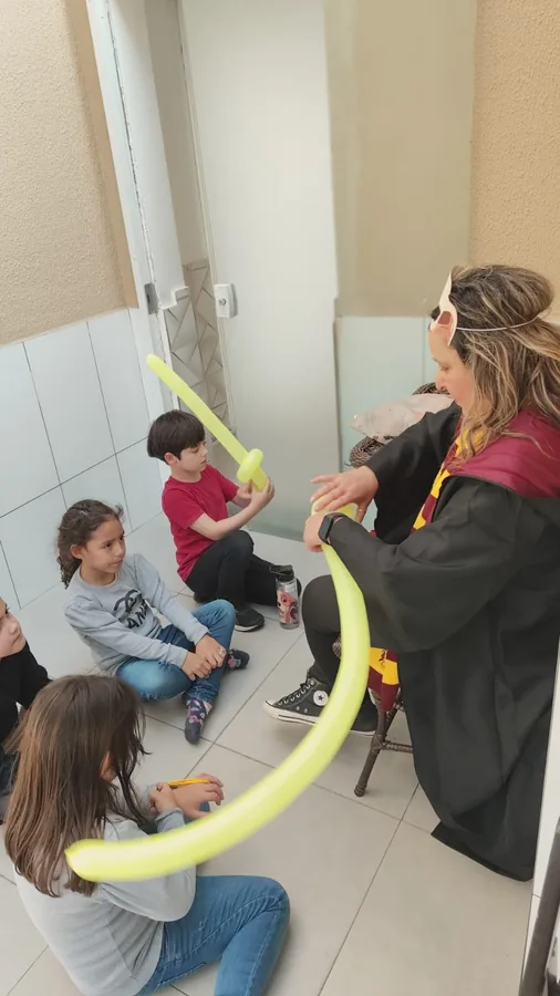 Recreadora fantasiada fazendo espadas de bexiga com as crianças